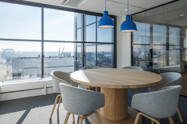 Vergaderruimte met ronde houten tafel, grijze stoelen en uitzicht op Rivium Quadrant in Rotterdam.